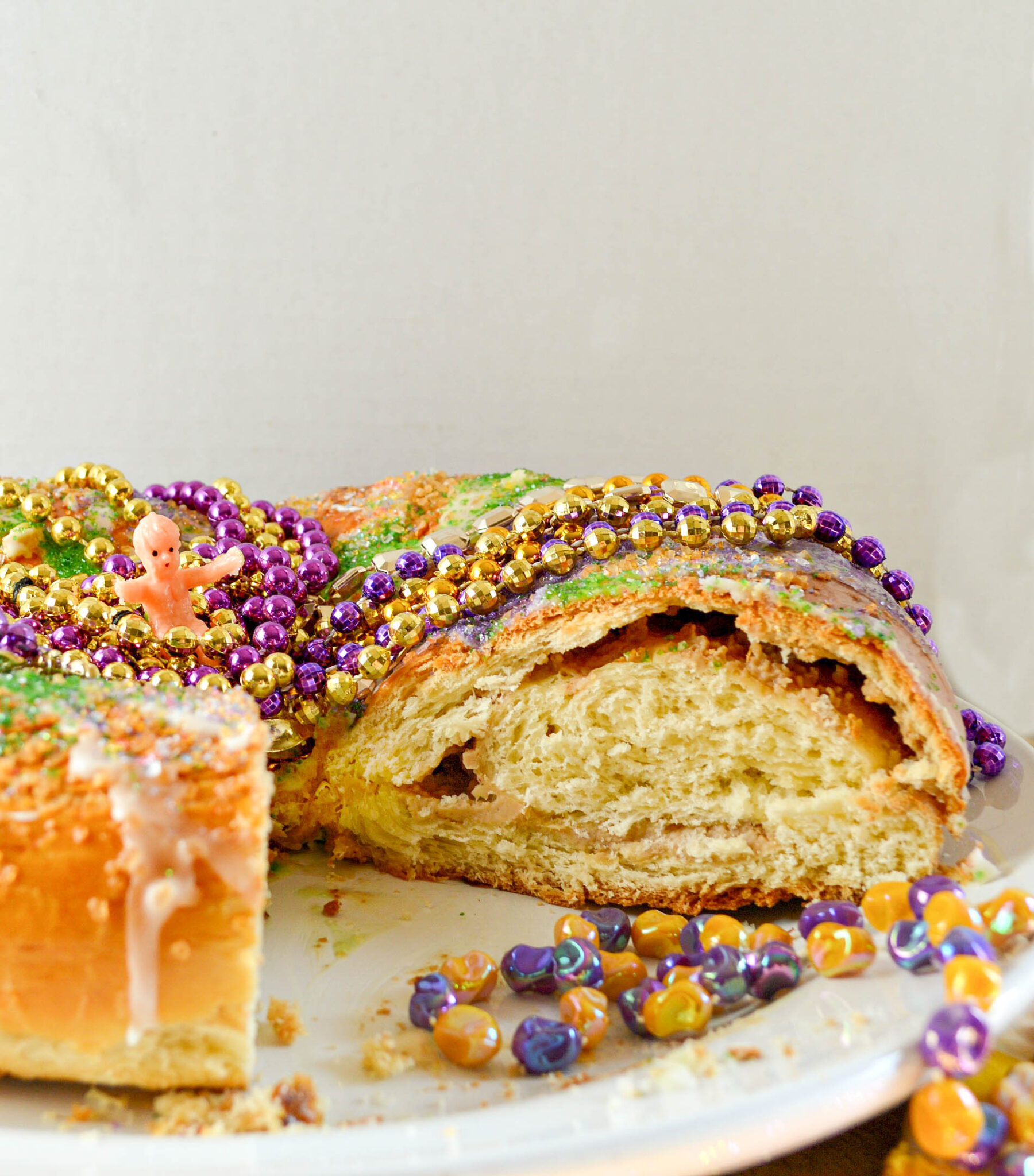 King Cake with cream cheese filling with colored sugar and mardi gras beads.