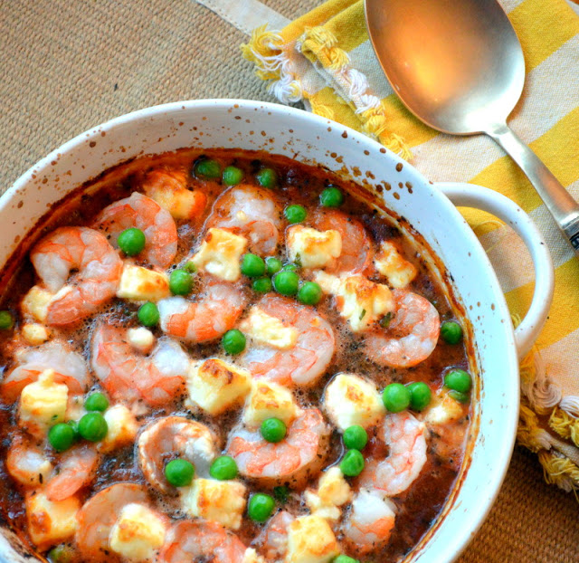 Greek Shrimp with Feta, Tomatoes and Green Peas in a white dish, yellow napkin and copper spoon