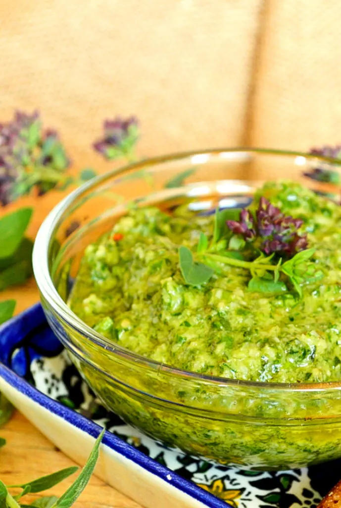 Green Lemon Oregano Pesto in clear bowl on blue tray on wood table.