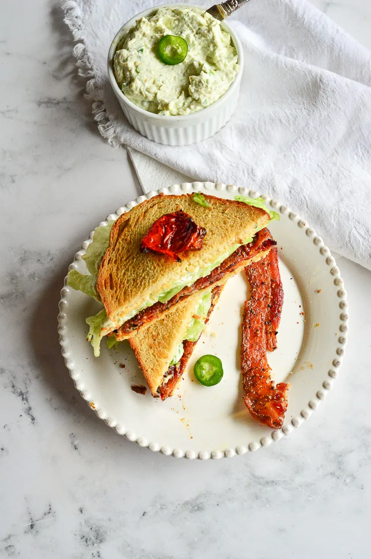 BLT sandwich on white plate cut in half with jalapeno cream cheese