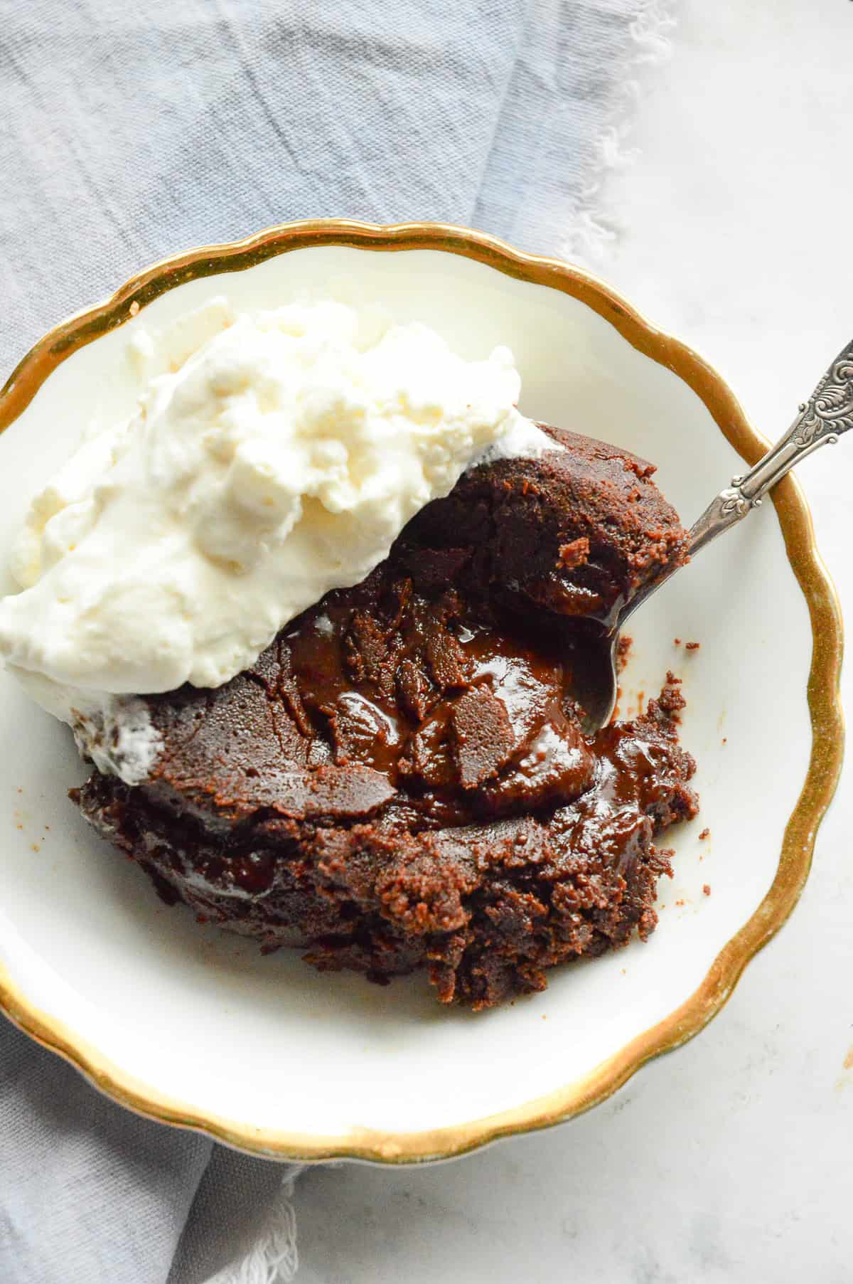 top down look of chocolate lava cake with whipped cream on gold rim plate with silver spoon