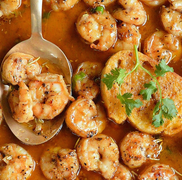 Barbecued shrimp in a buttery red sauce with a spoon scooping out shrimp and green parsley on top.