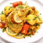 saffron chicken on white plate with carrots and lemon