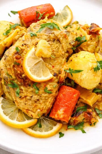 saffron chicken on white plate with carrots and lemon