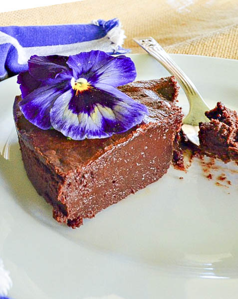 passover chocolate cake recipe on white plate garnished with purple pansy