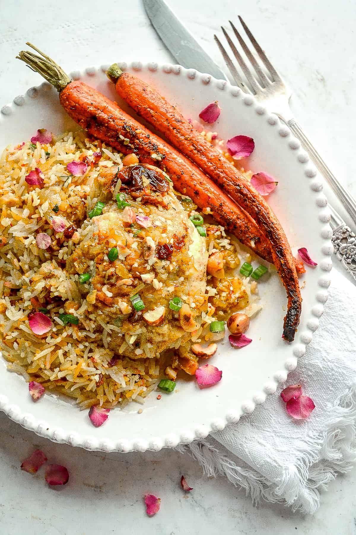 chicken with saffron, hazelnuts and honey on white plate with roasted carrots and rice and knife and fork