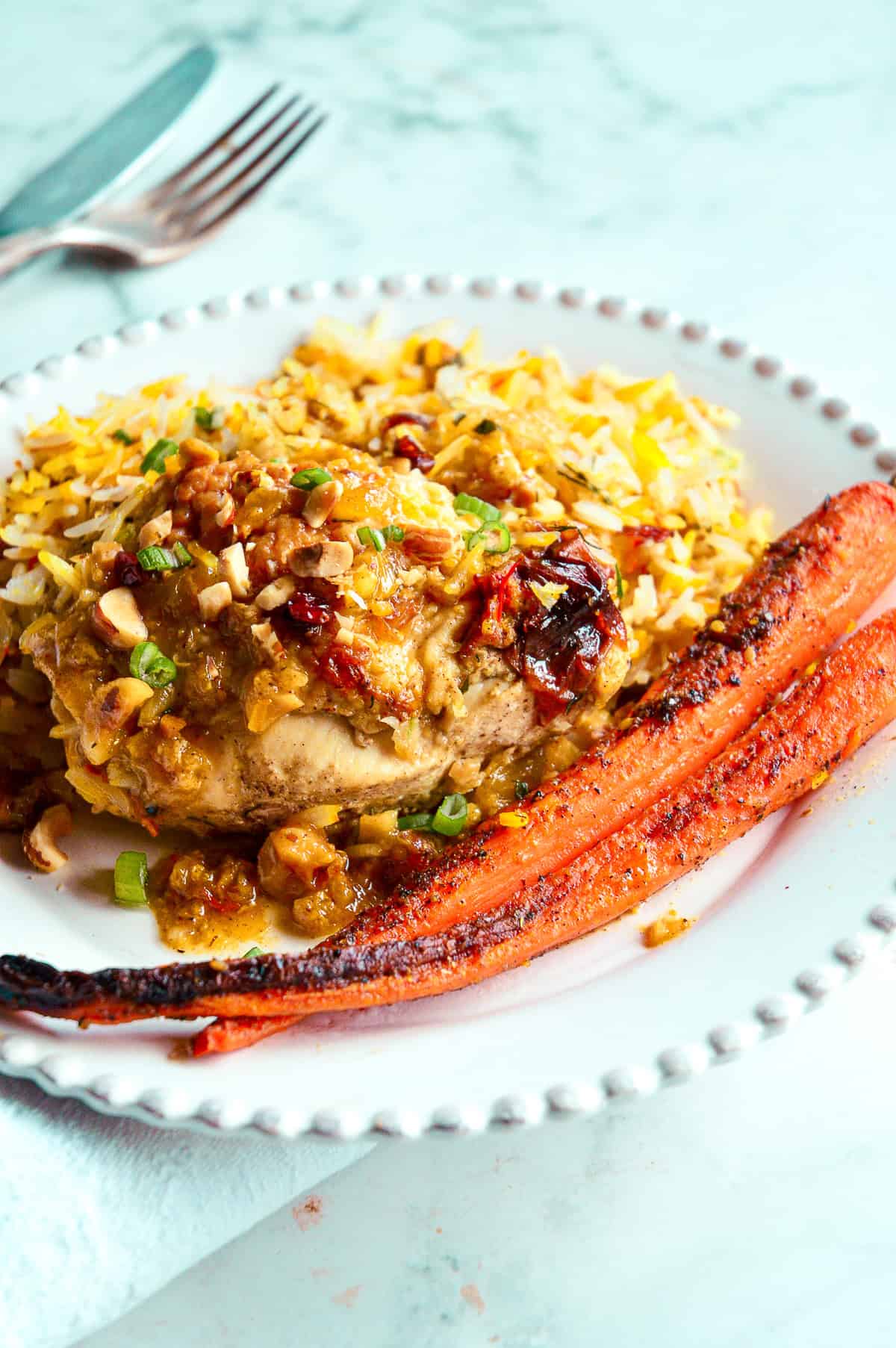 marinated roast chicken with saffron, hazelnuts and honey on white dinner plate with roasted carrots and saffron rice
