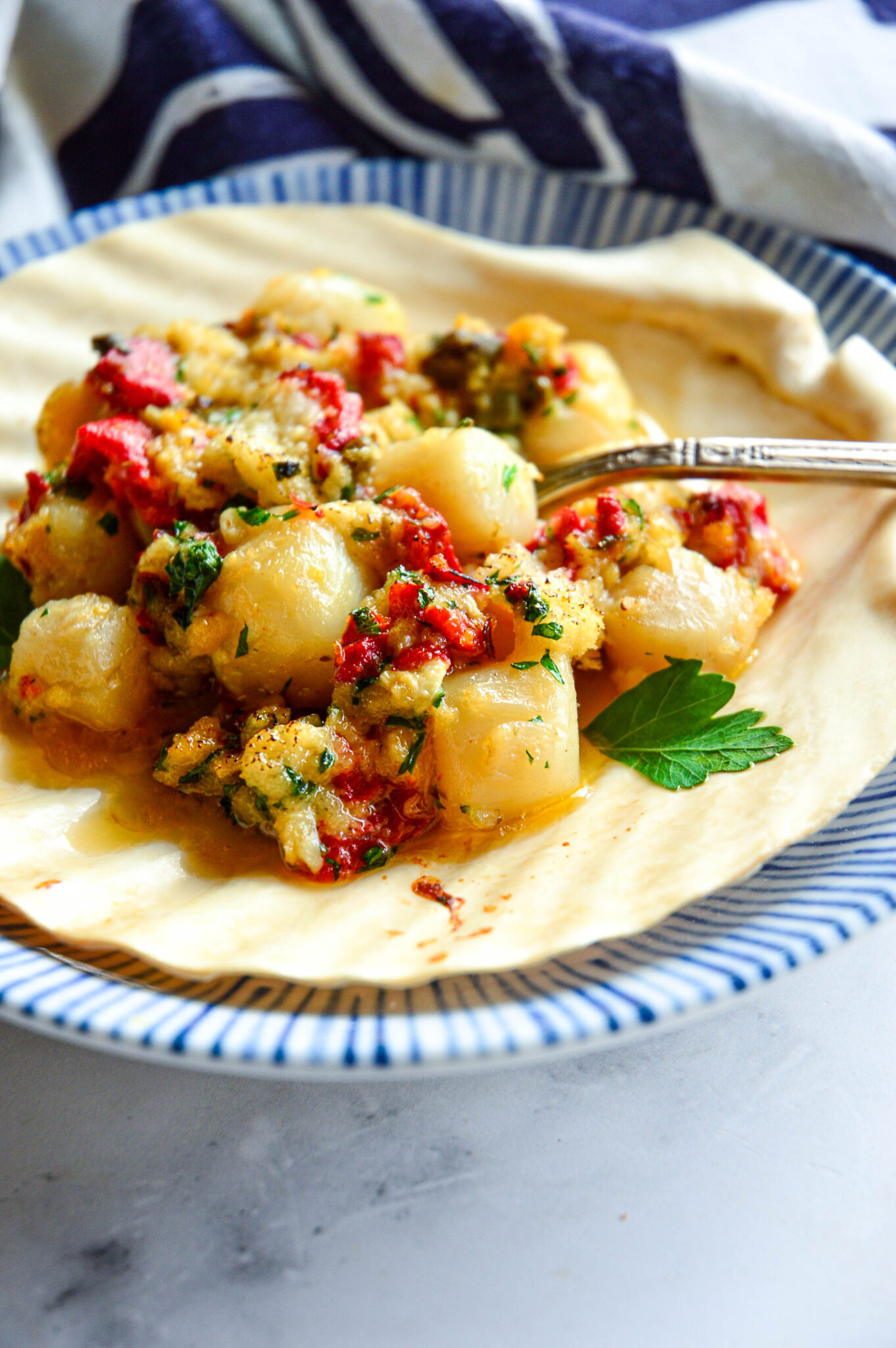 bay scallops with lemon, garlic and red peppers in scallop shell on bue striped plate