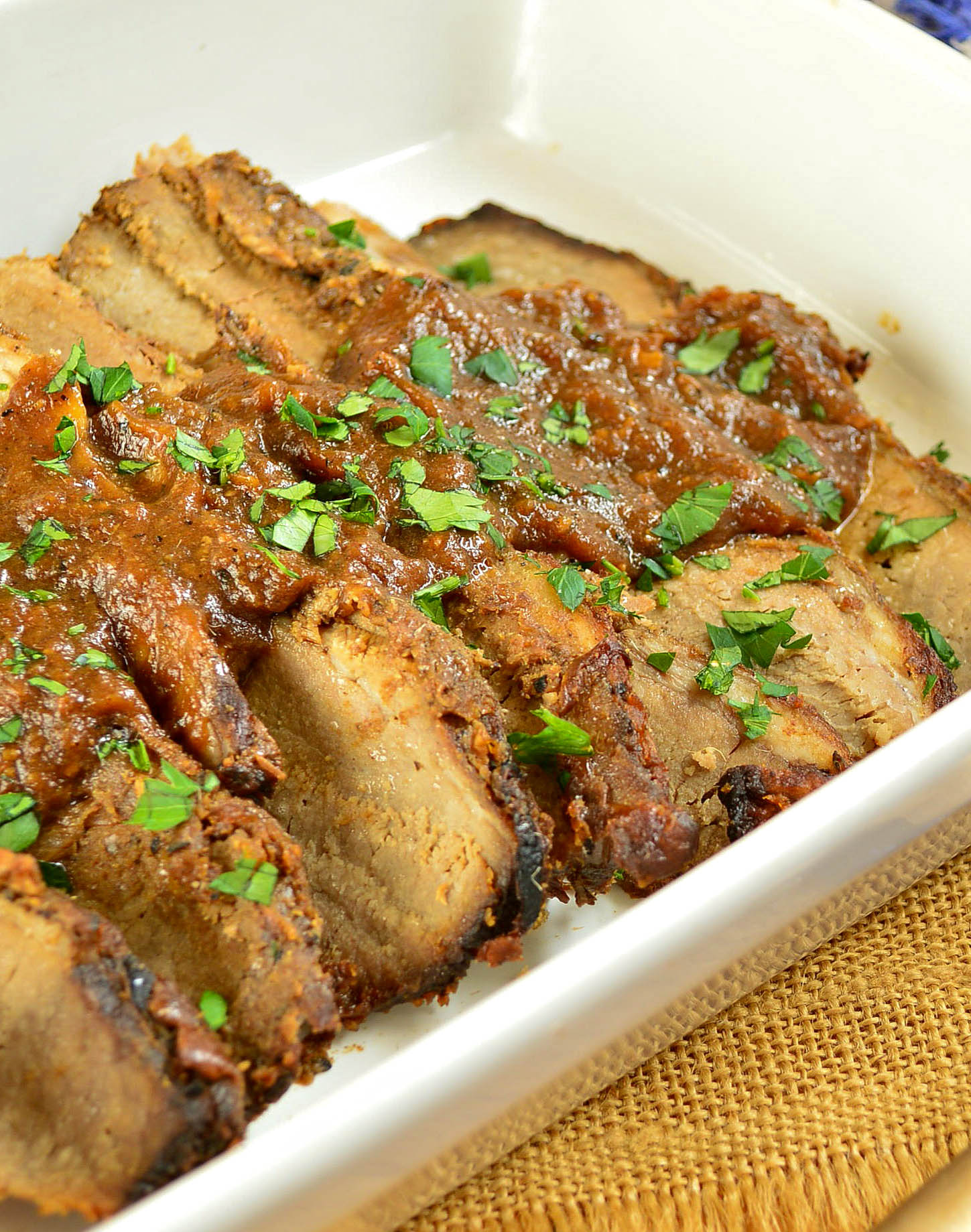 brisket with red sauce on top in a white pan.