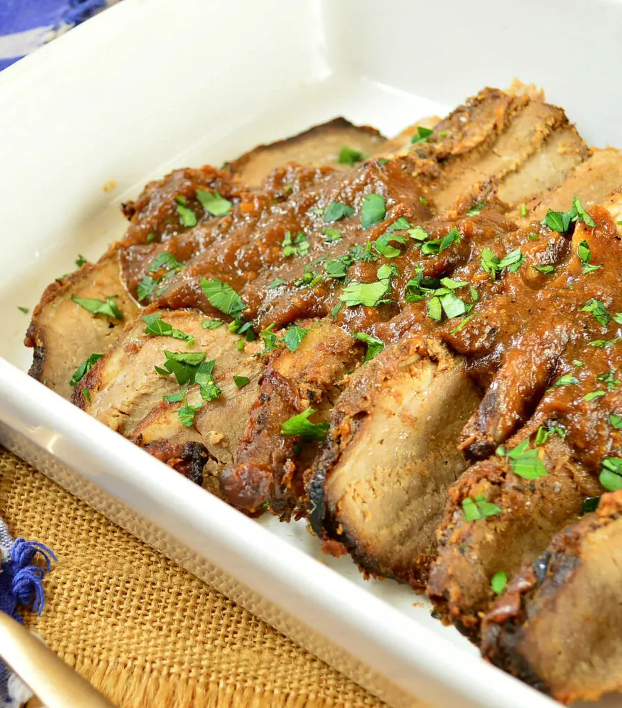 brisket with red sauce on top in a white pan.