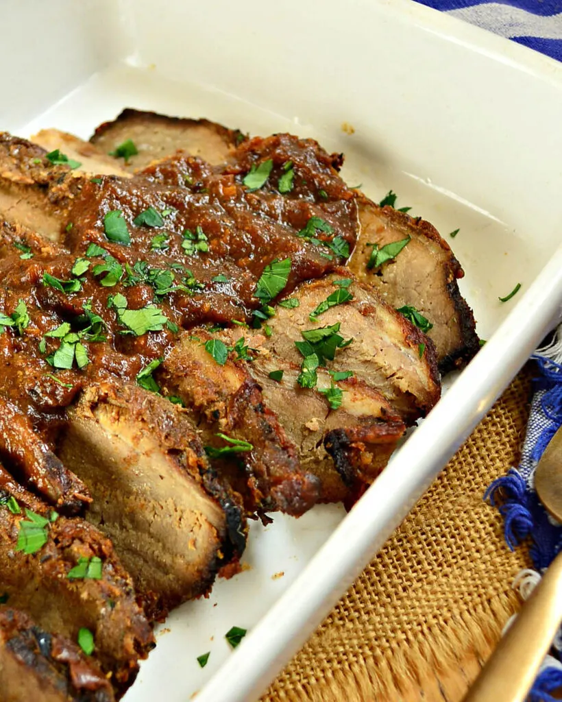 brisket with red sauce on top in a white pan.