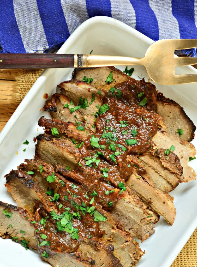 brisket with red sauce on top in a white pan.