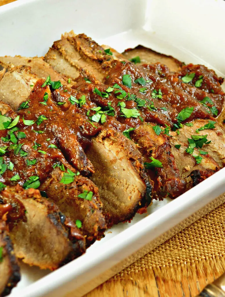 brisket meat with red sauce on top in a white pan.