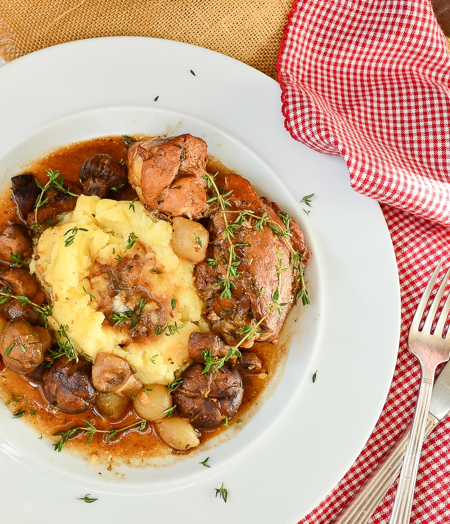 chicken in red wine on white plate with checked napkin