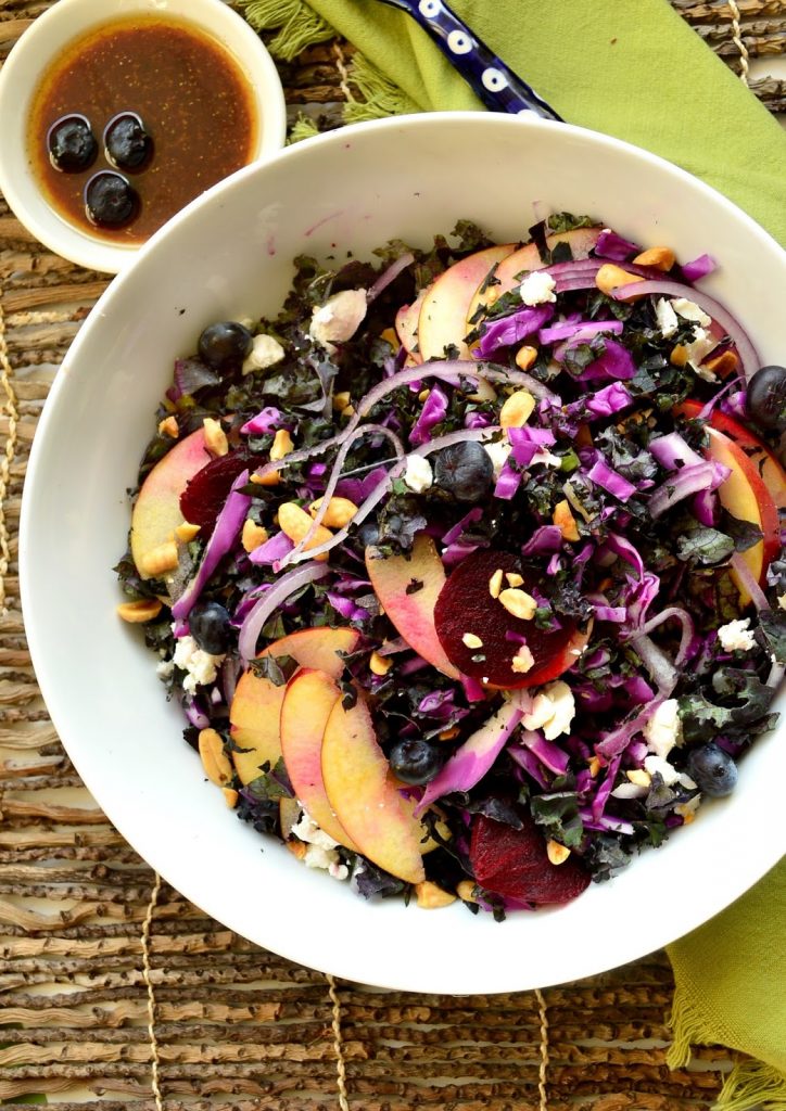purple kale salad in white bowl with small bowl of blueberry vinaigrette