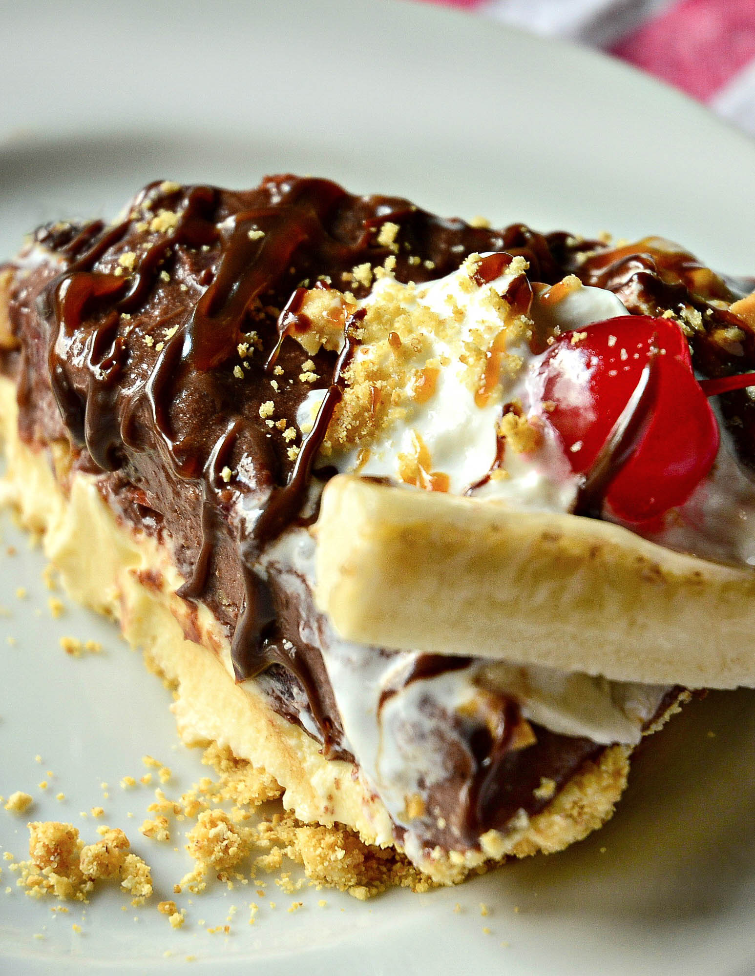 piece of pie with crumble base, creamy middle, and chocolate, nuts, cherry and whipped cream on top.