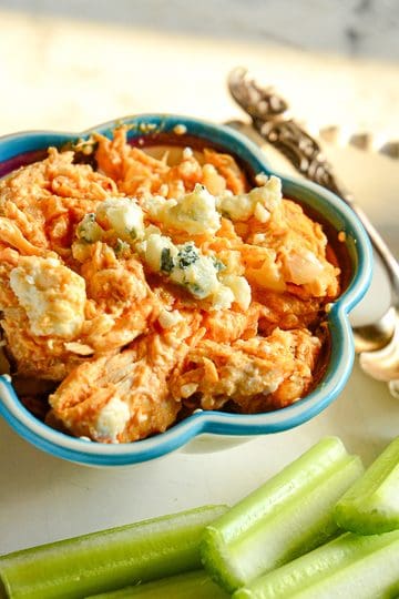 buffalo chicken dip in small bowl with celery and serving spoon and topped with blue cheese