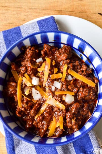 cincinnati chili in blue striped bowl with cheese and onions
