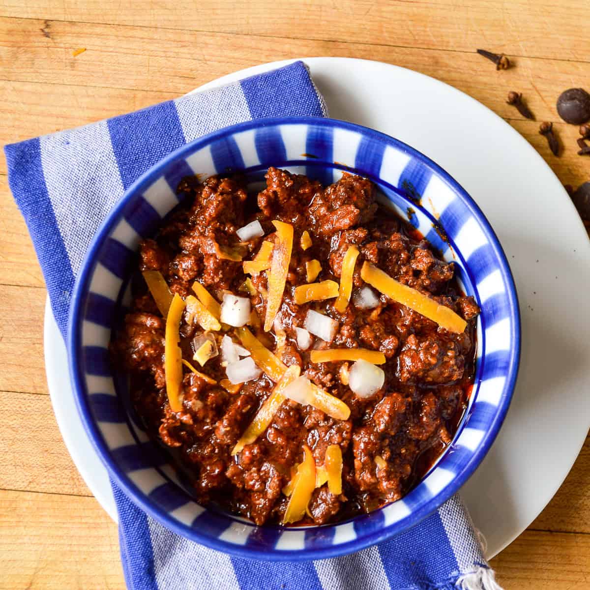cincinnati chili in blue striped bowl with blue striped napkin on white plate