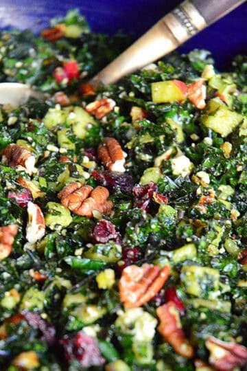 kale salad in blue bowl with pecans and dried cranberries