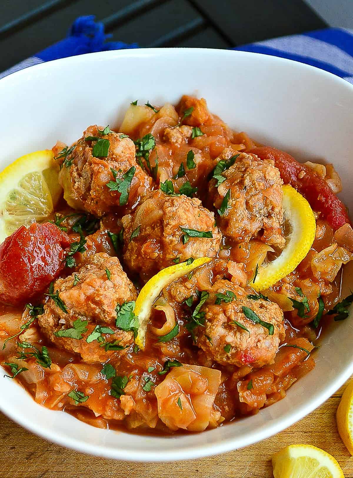 meatballs with sweet and sour cabbage in white bowl with lemons