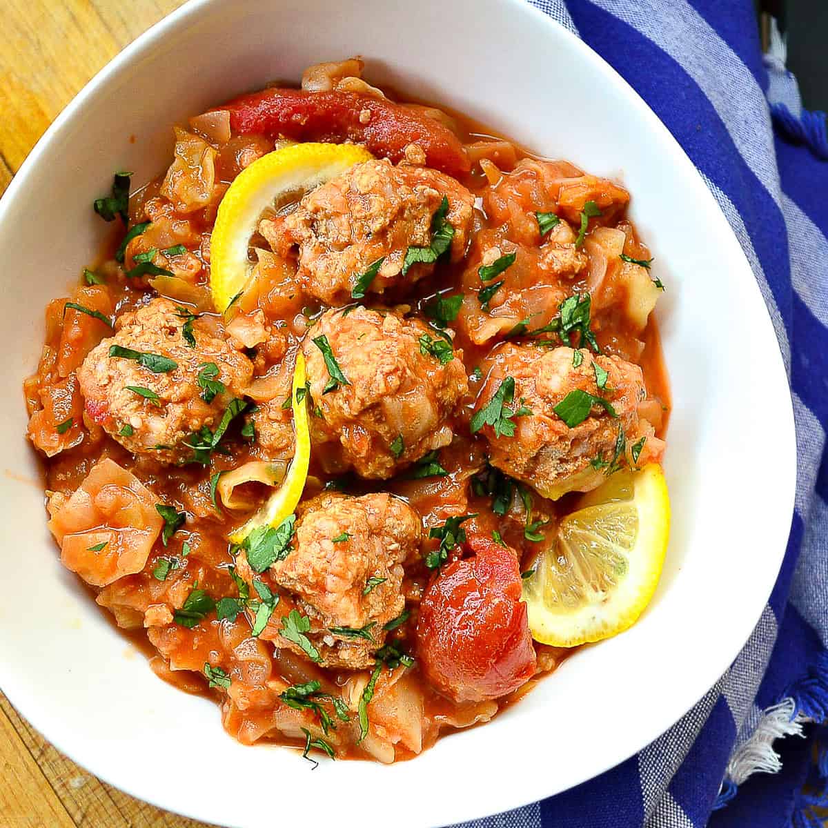 unstuffed sweet and sour cabbage with meatballs in white bowl with lemons