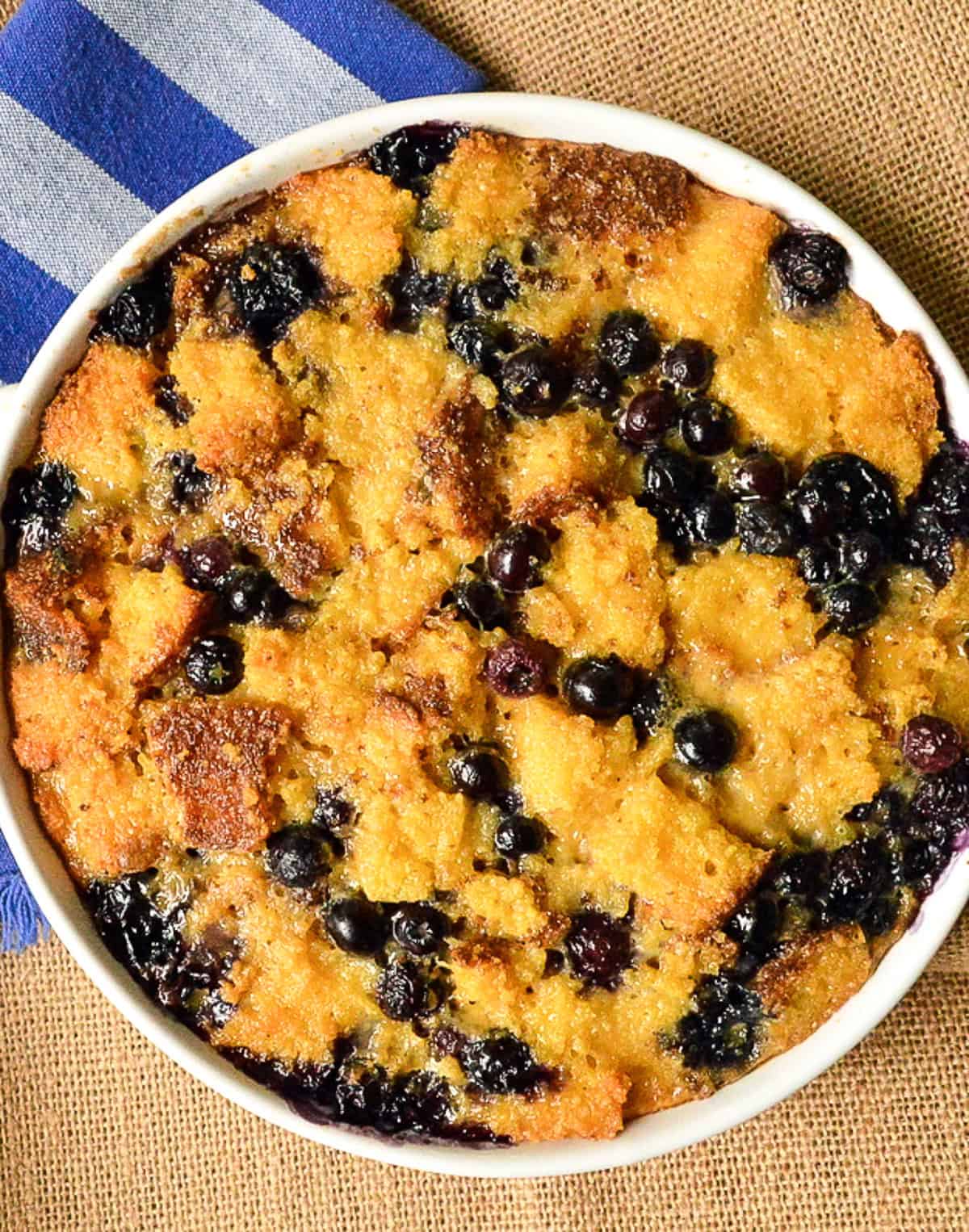 cornbread bread pudding with blueberries in a white ceramic baking dish with blue striped napkin