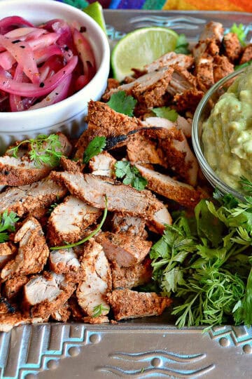 Marinated grilled pork tenderloin on mexican platter with avocado cream and pickled onions