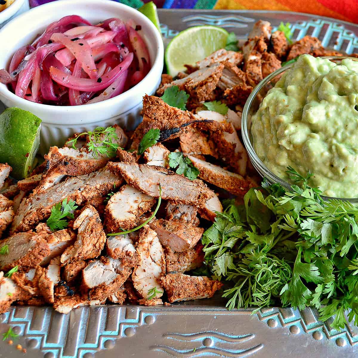 Marinated grilled pork tenderloin with pickled onions and avocado cream on mexican platter