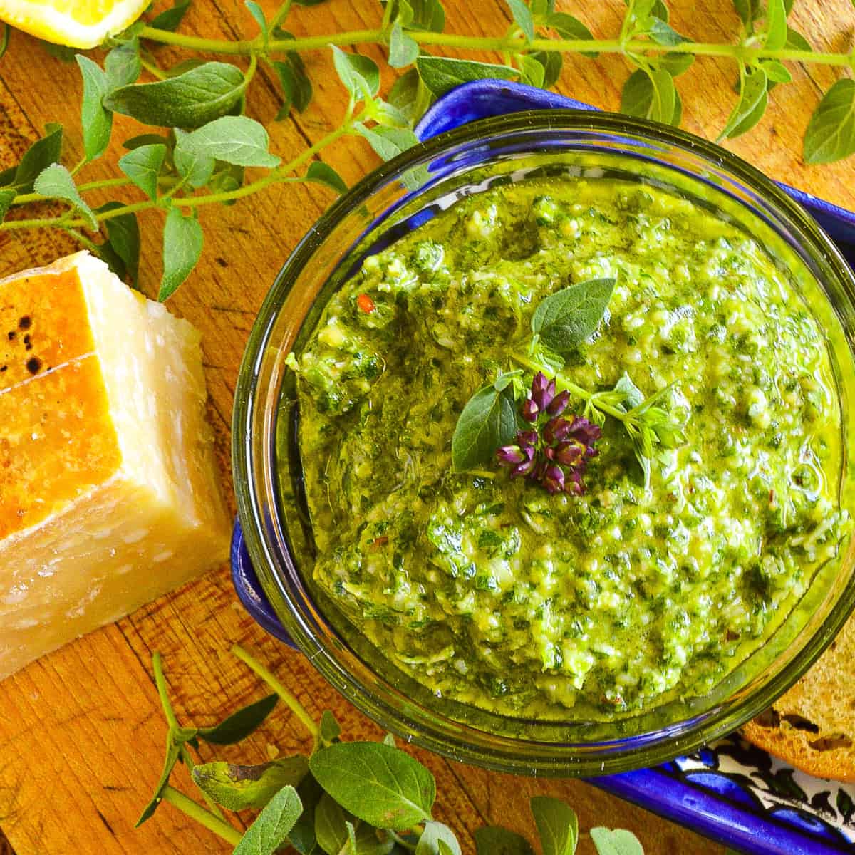 bright green lemon oregano pesto with wedge of parmesan and fresh oregano leaves on cuttin board, garnished with purple oregano flower