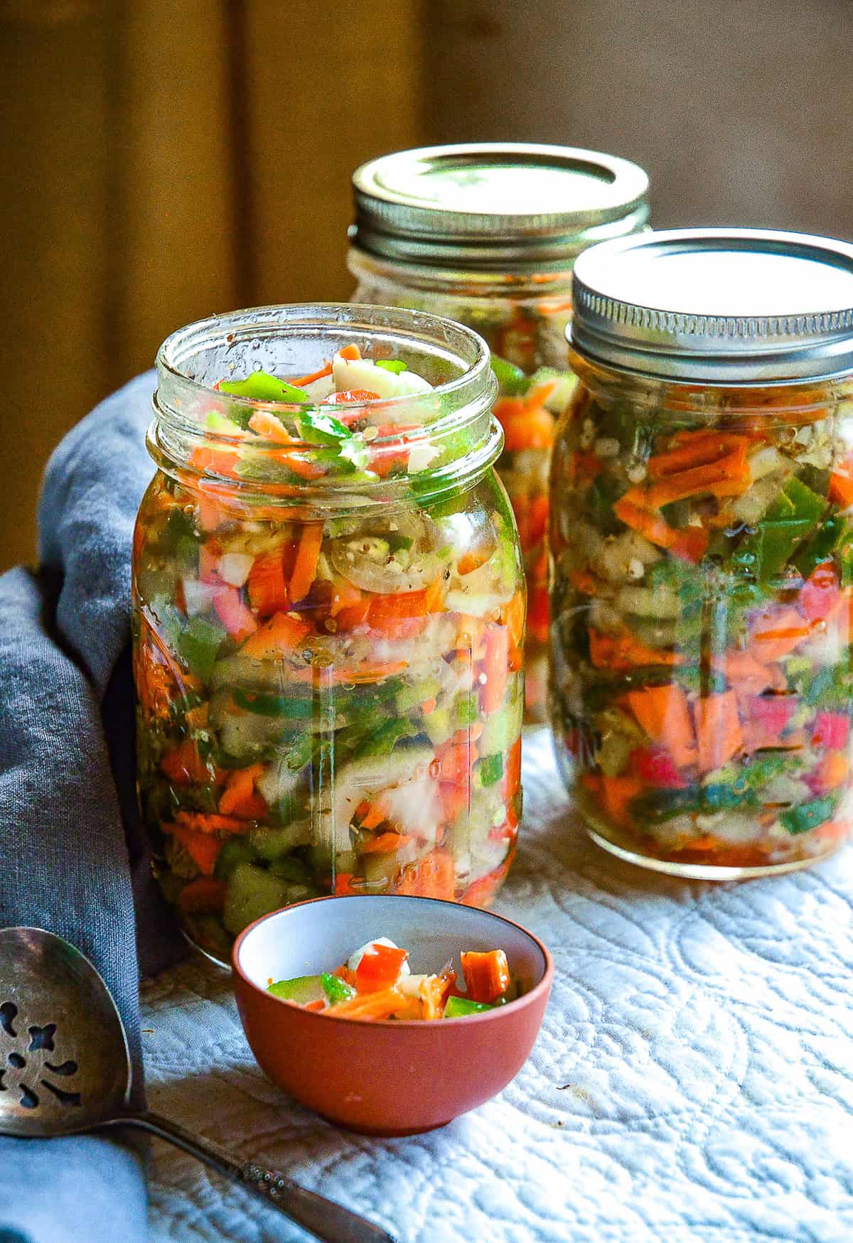 chicago style giardinera in mason jars with serving spoon contains carrots, jalapenos, peppers and celery, in an oil based italian dressing