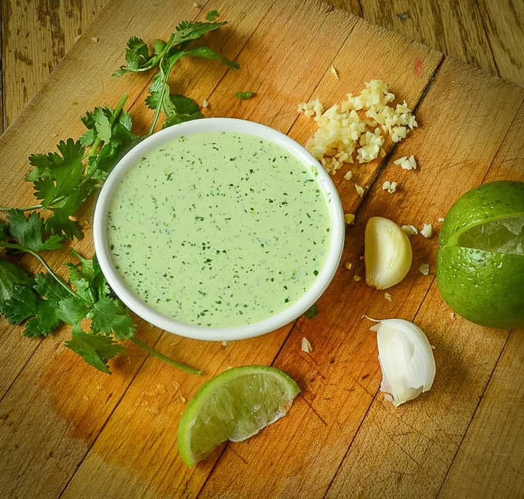 peruvian green sauce on wood board with garlic, lime and cilantro