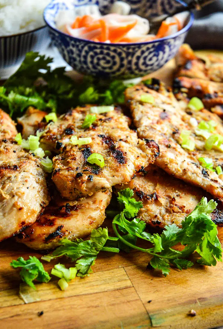 Grilled Chicken on brown cutting board with green parsley.