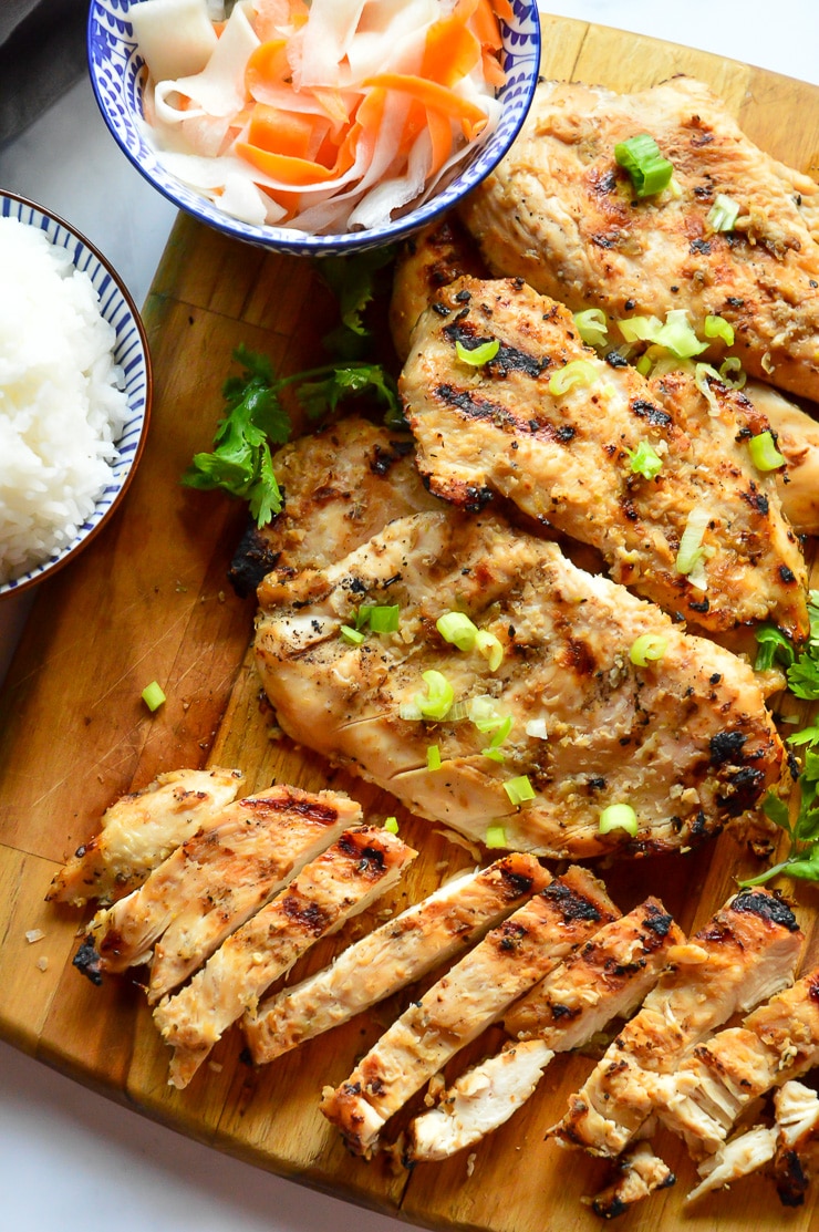 grilled chicken on cutting board with shaved carrots and rice in bowls.