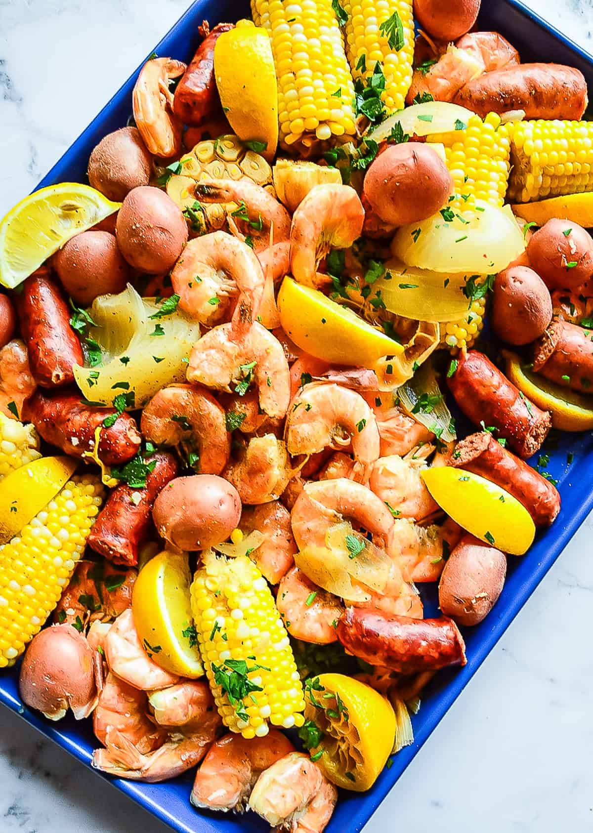 shrimp boil with corn on the cob, sausage and potatoes on blue sheet pan