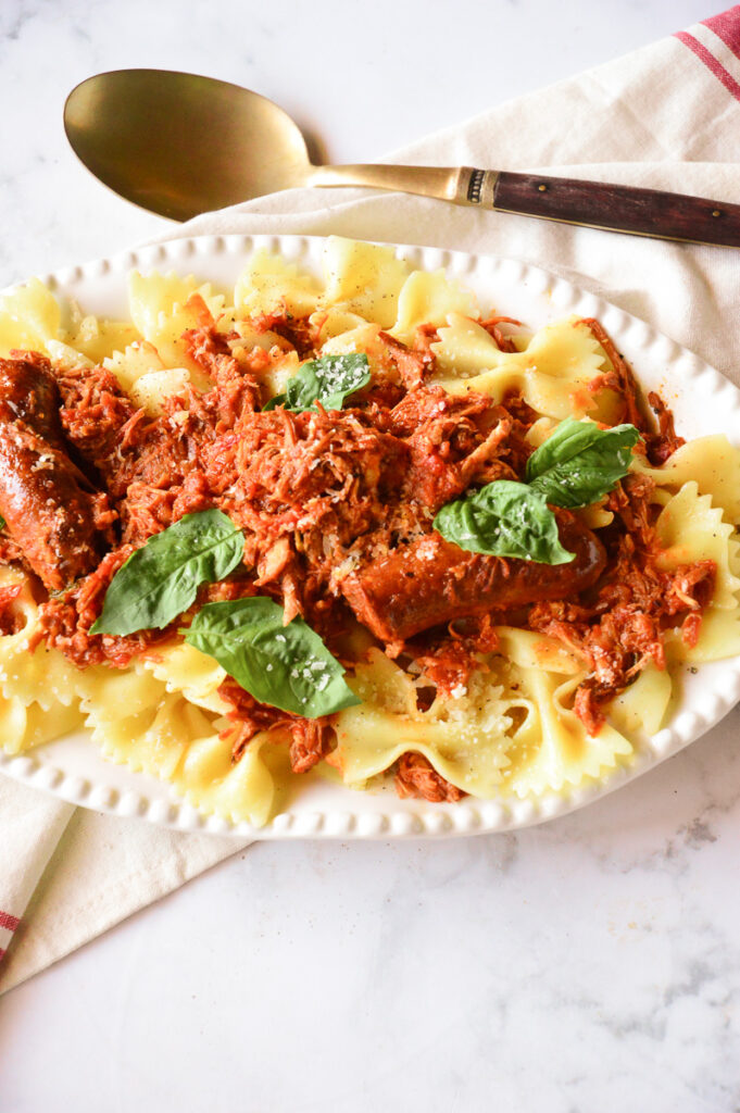 Pork ragu over bowtie pasta on white platter with serving spoon