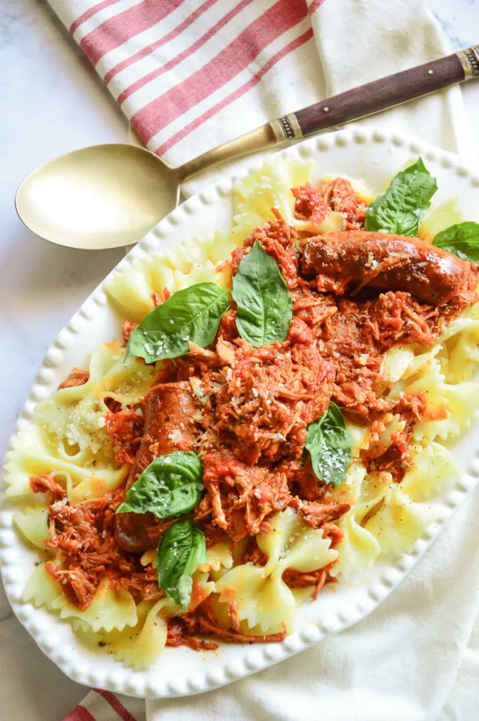 Pork Ragu sauce over pasta on white platter with serving spoon and striped red towel