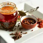 Chinese chili garlic oil in jar with star anise, sichuan peppercorns on white plate