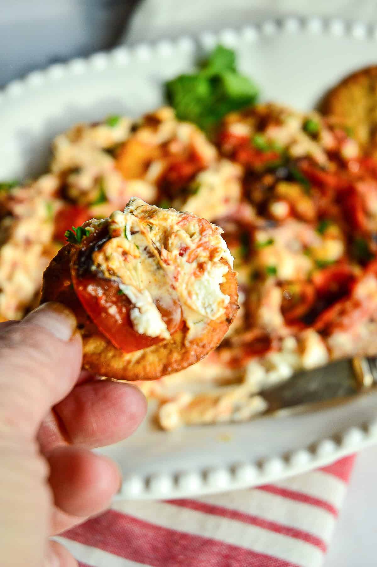boursin cheese dip with roasted tomatoes on cracker held by hand