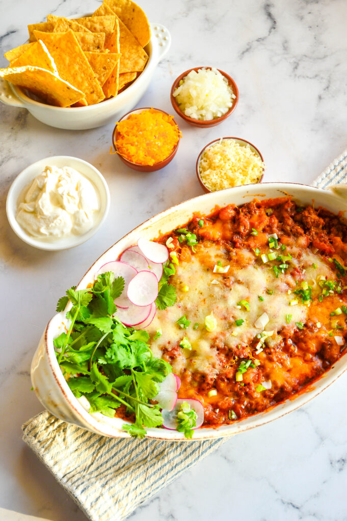 chicken taco casserole in ceramic white baking dish with toppings in bowls