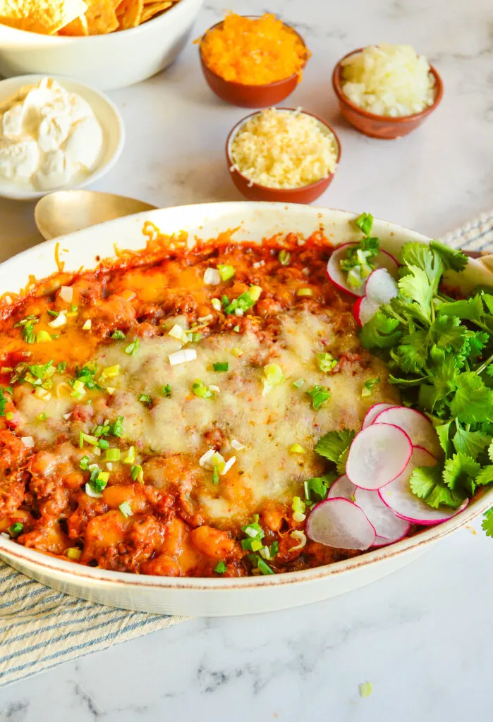 chicken taco casserole in white baking dish with bowls in toppings