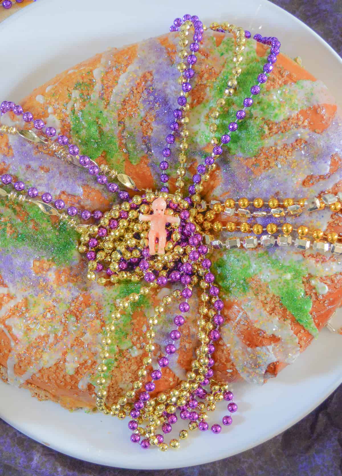 king cake with cream cheese filling topped with plastic baby and Mardi Gras beads