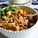 Thai garlic pepper chicken recipe in white bowl iwht rice in blue bowl in background