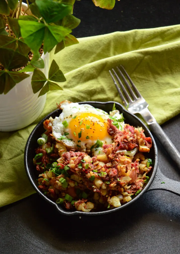 easy corned beef hash breakfast recipe in cast iron skiller with fork and green napkin