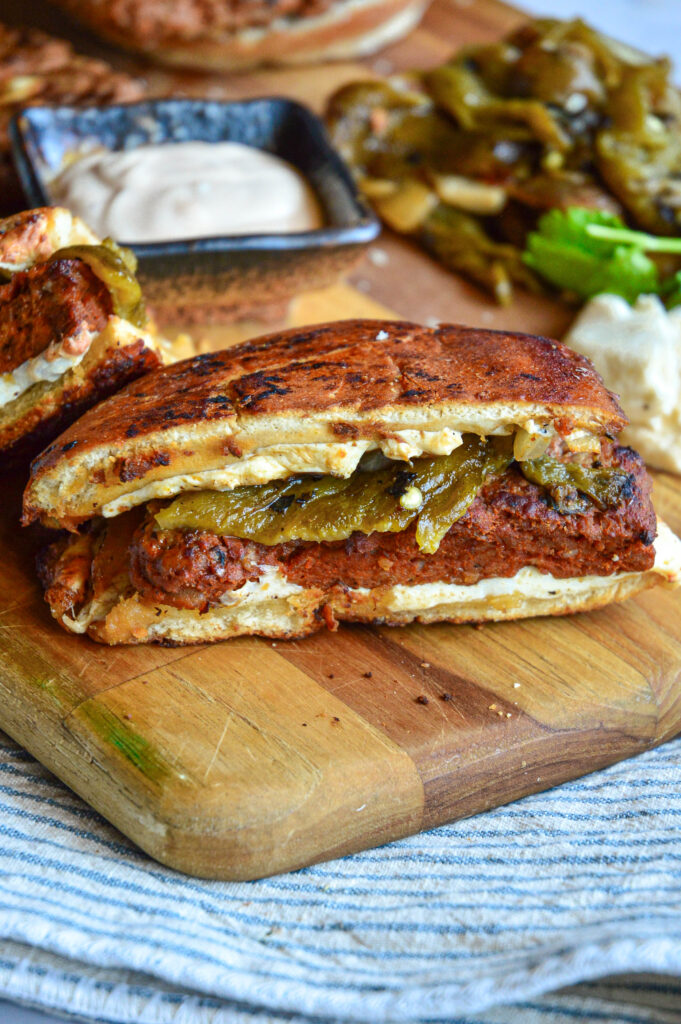 chorizo recipe ideas featuring a chorizo burger with green chiles and cheese on a cuttin board with mayo and green chiles