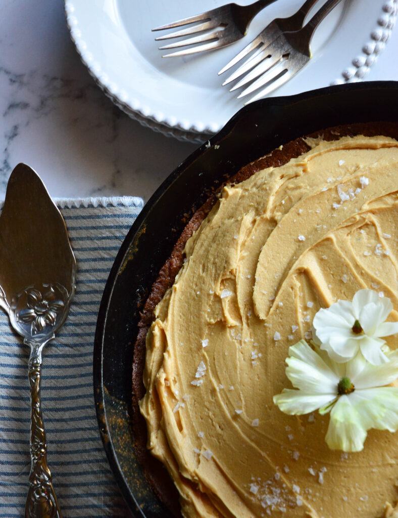 apple skilet cake with salted caramel frosting in skillet with dessert dishes