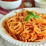spaghetti on plate with Italian red sauce recipe in background
