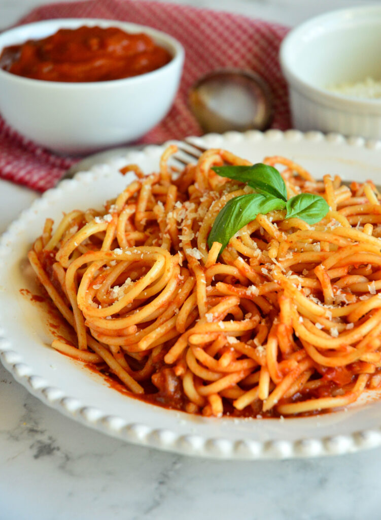 spaghetti on plate with Italian red sauce recipe in background