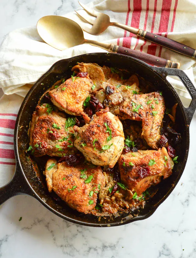 garlic braised chicken thighs recipe in cast iron skillet with cherries and servingware