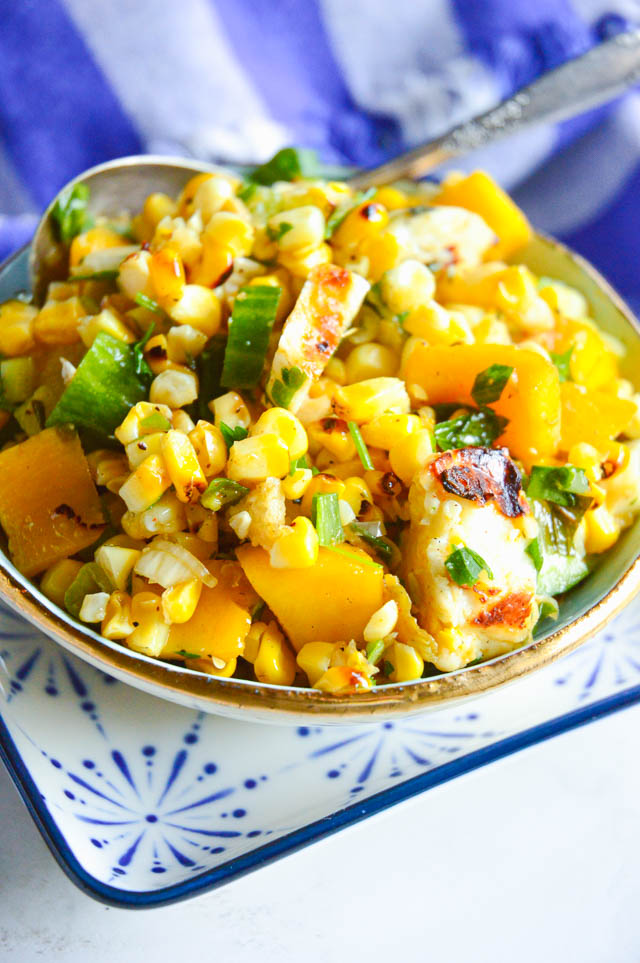 grilled corn salad in bowl with cheese, cucumbers and mango with silver spoon